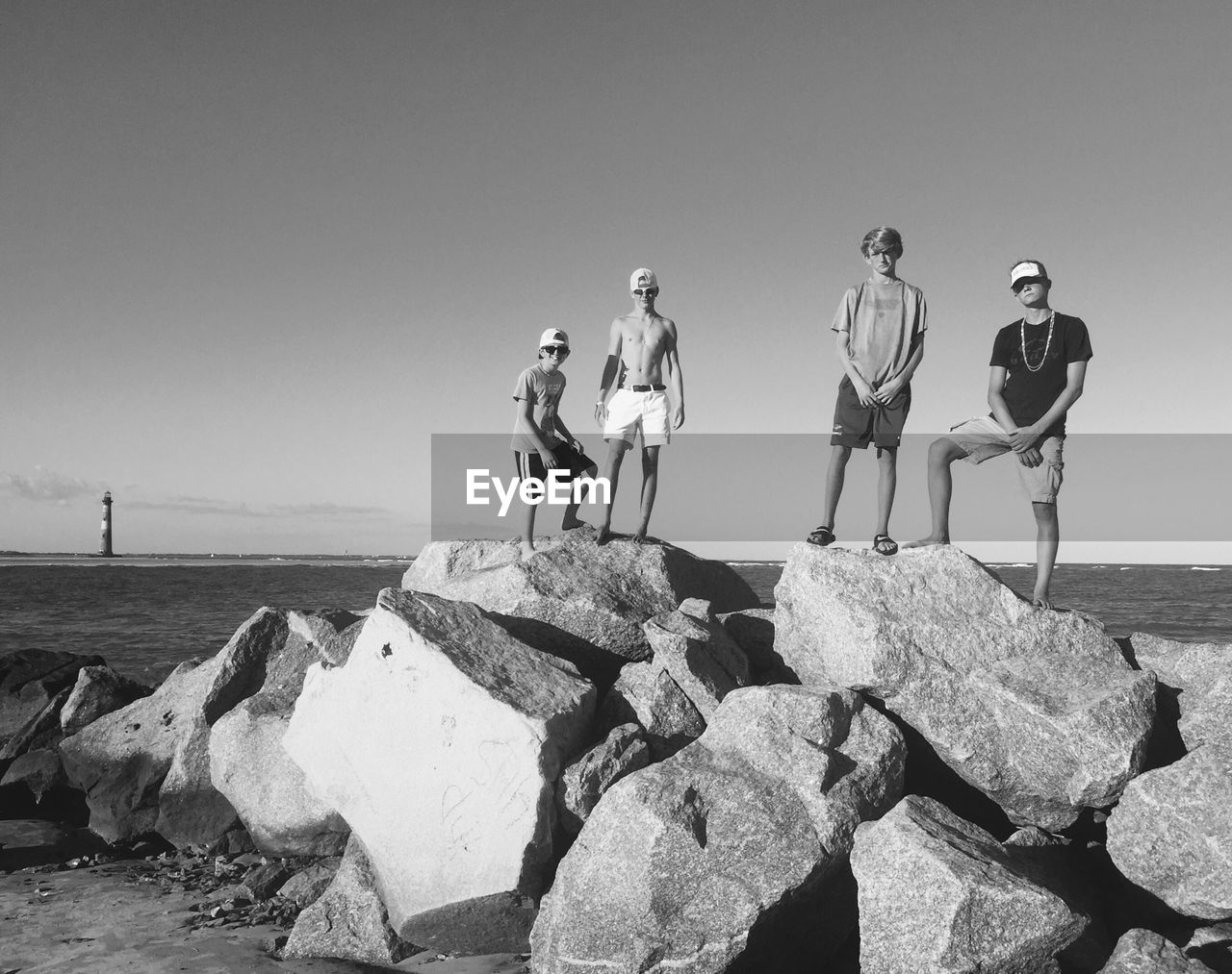 PEOPLE STANDING ON ROCK AT BEACH AGAINST CLEAR SKY