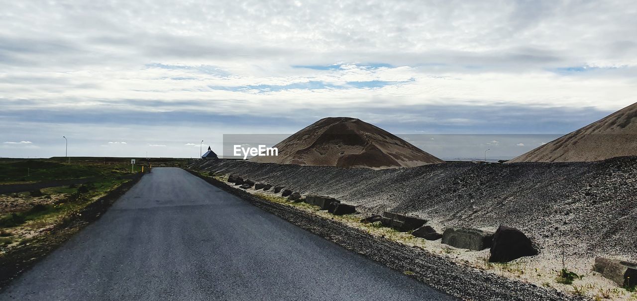 Road leading towards mountain against cloudy sky