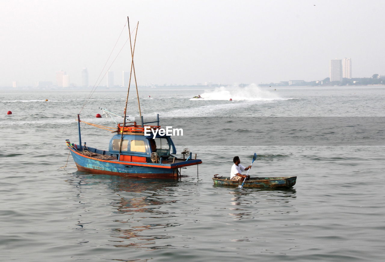 REAR VIEW OF MAN IN BOAT SAILING ON SEA