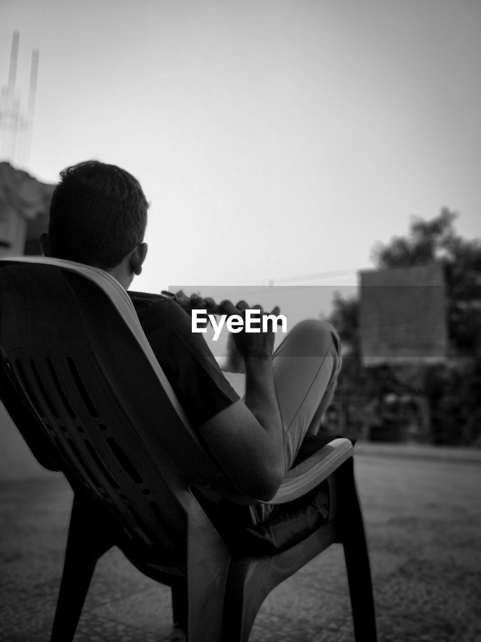 Rear view of man sitting on chair playing flute against clear sky