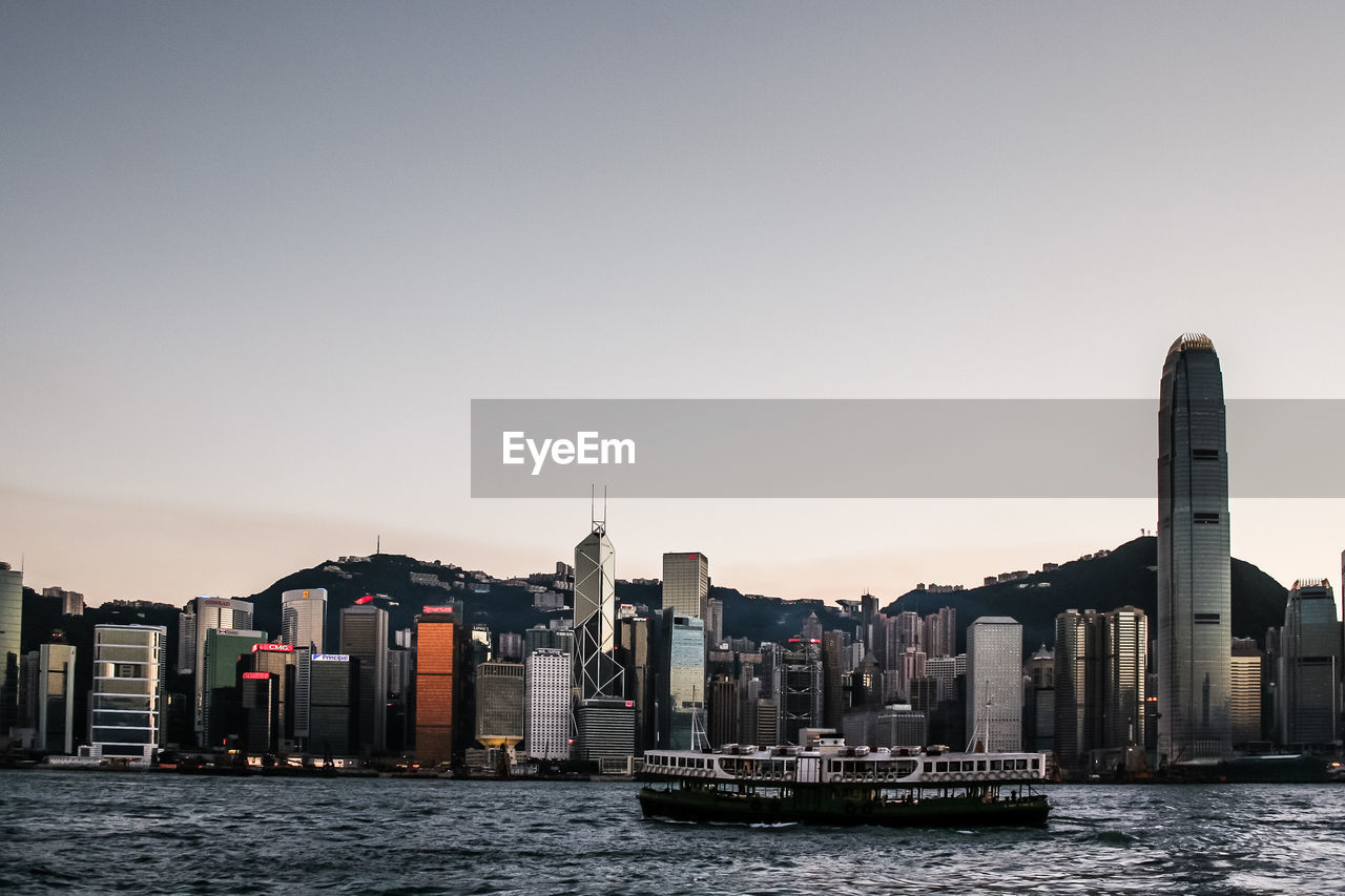 Ferry sailing on victoria harbor against two international finance center at sunset