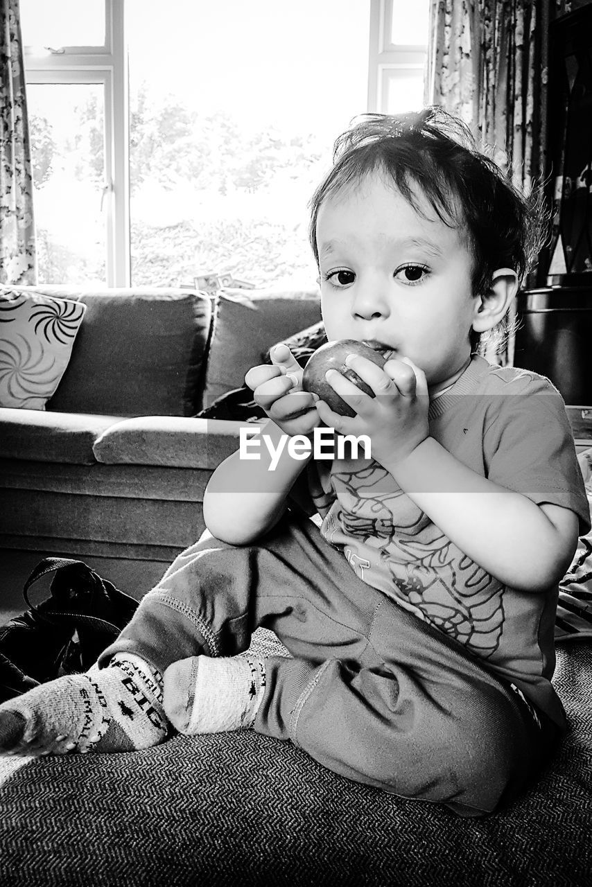 Portrait of cute boy eating fruit at home