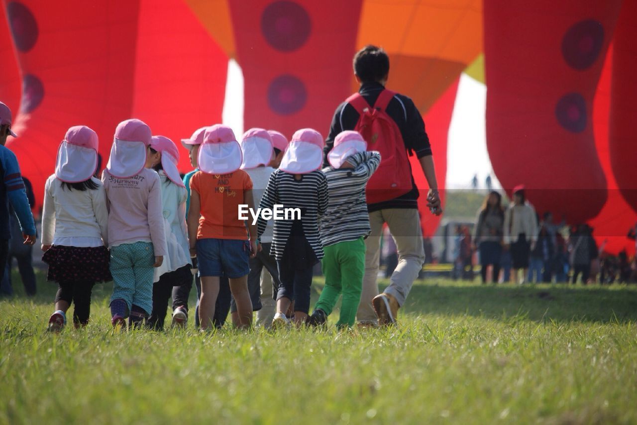 Full length rear view of man with children walking on grassy field against hot air balloons