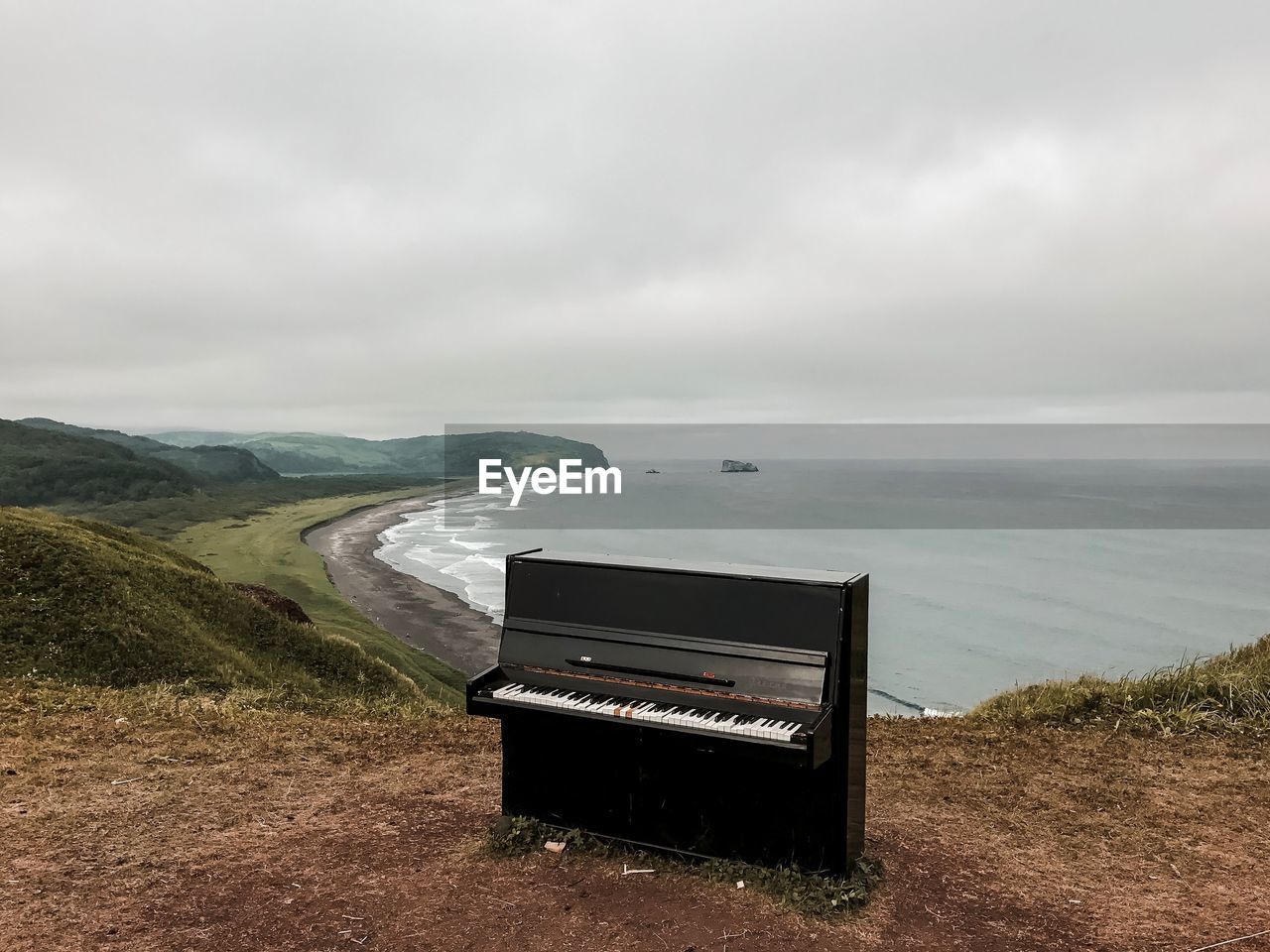 Piano on mountain by sea against cloudy sky