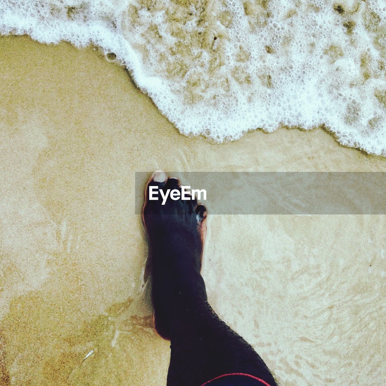 Low section of person with black paint standing at beach