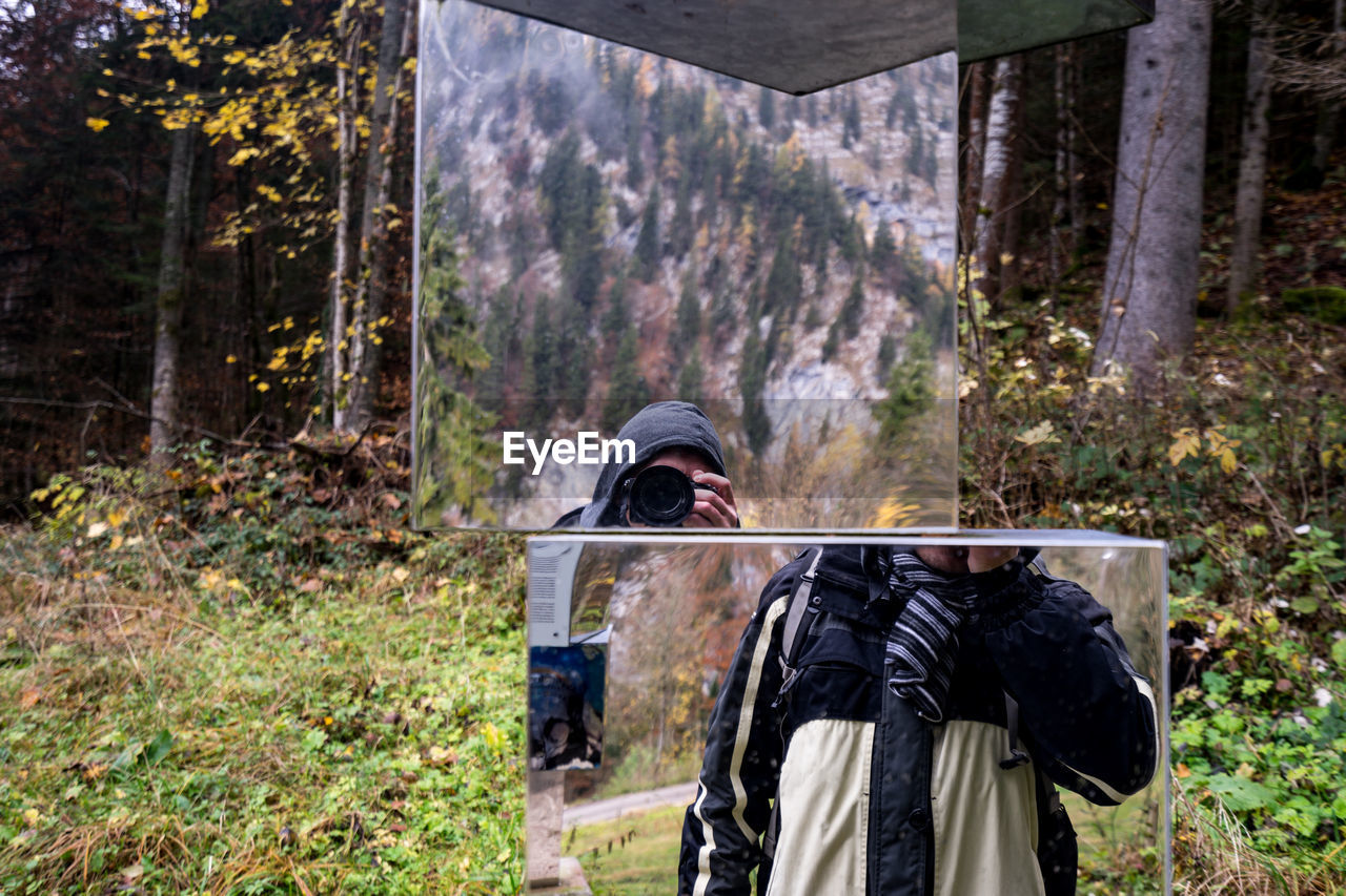 Reflection of man photographing on glass in forest