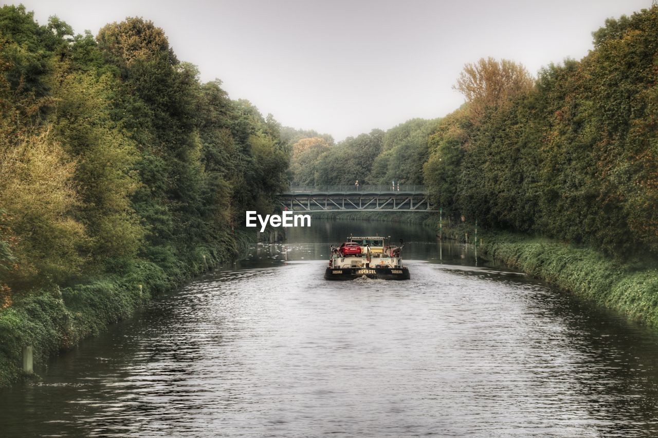 Boat sailing on river amidst trees against sky