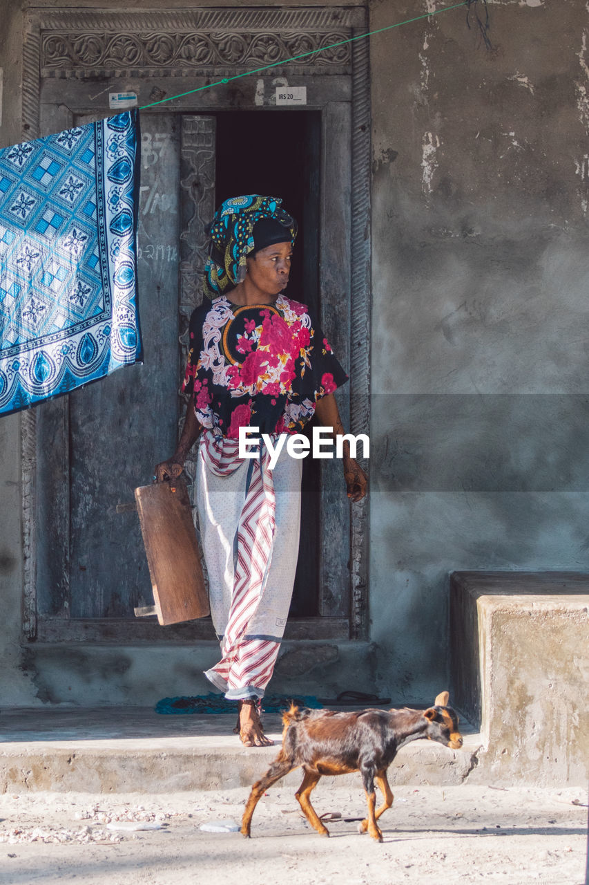 one person, full length, women, architecture, adult, clothing, animal, animal themes, dog, domestic animals, female, lifestyles, one animal, mammal, person, building exterior, street, day, pet, built structure, blue, traditional clothing, outdoors, fashion, temple, building, standing, nature, city, spring, casual clothing, portrait, front view, young adult, road, wall - building feature, carnivore, walking