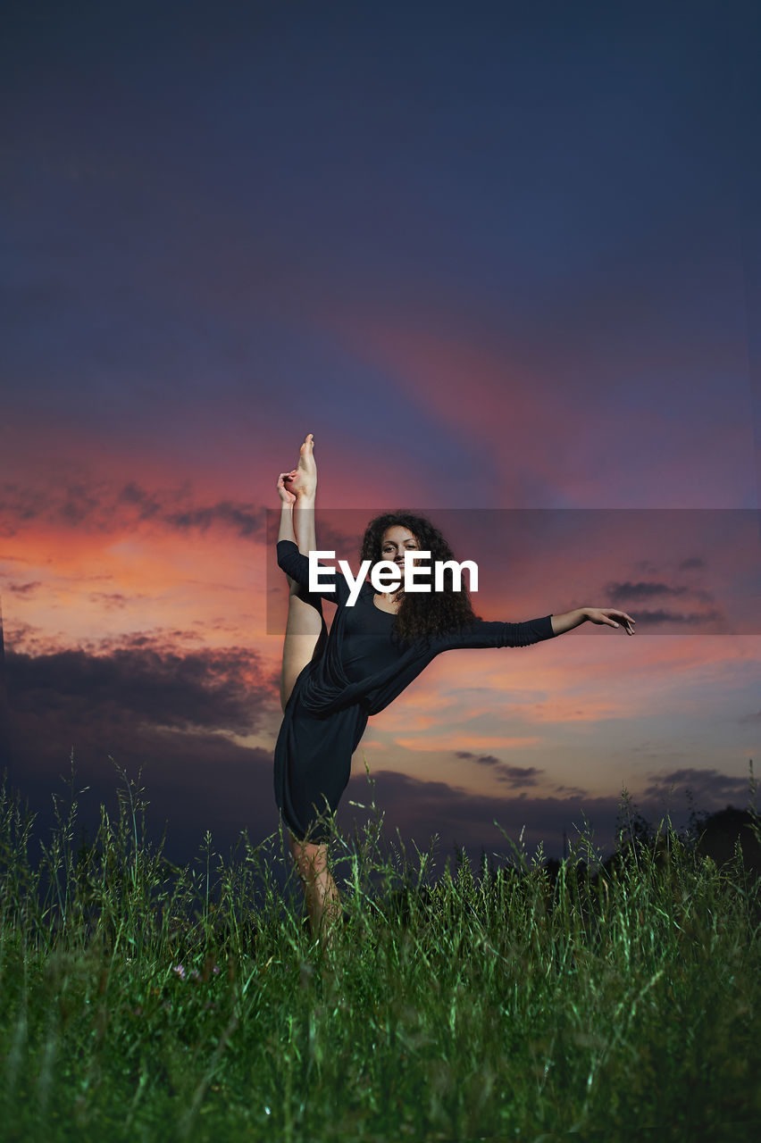 Woman standing on field against sky during sunset