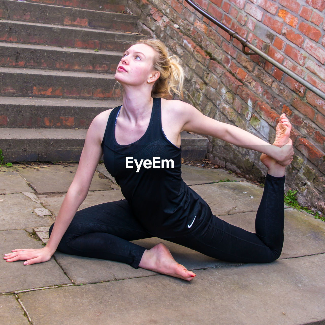 Young woman stretching on steps against brick wall