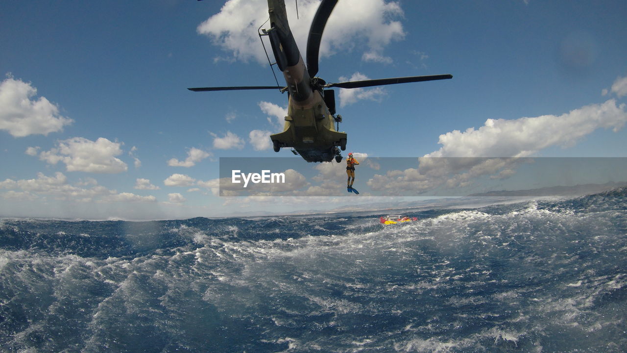 Person jumping in sea from helicopter against sky