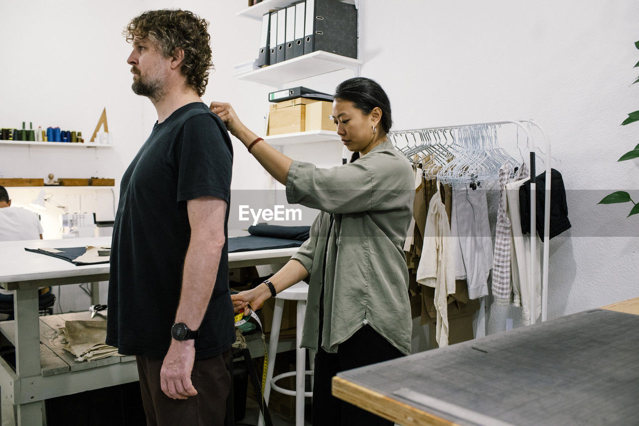 Female tailor taking measures of male customer at workshop