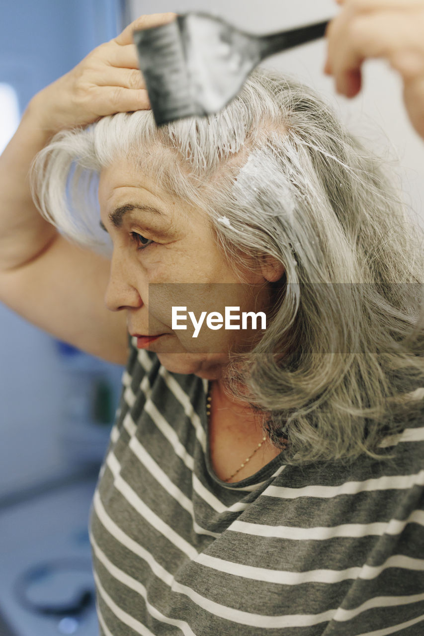 Senior woman applying dye with hairbrush at home