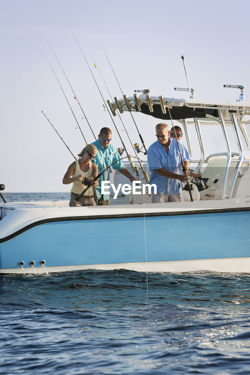 Friends fishing on boat at sea against sky