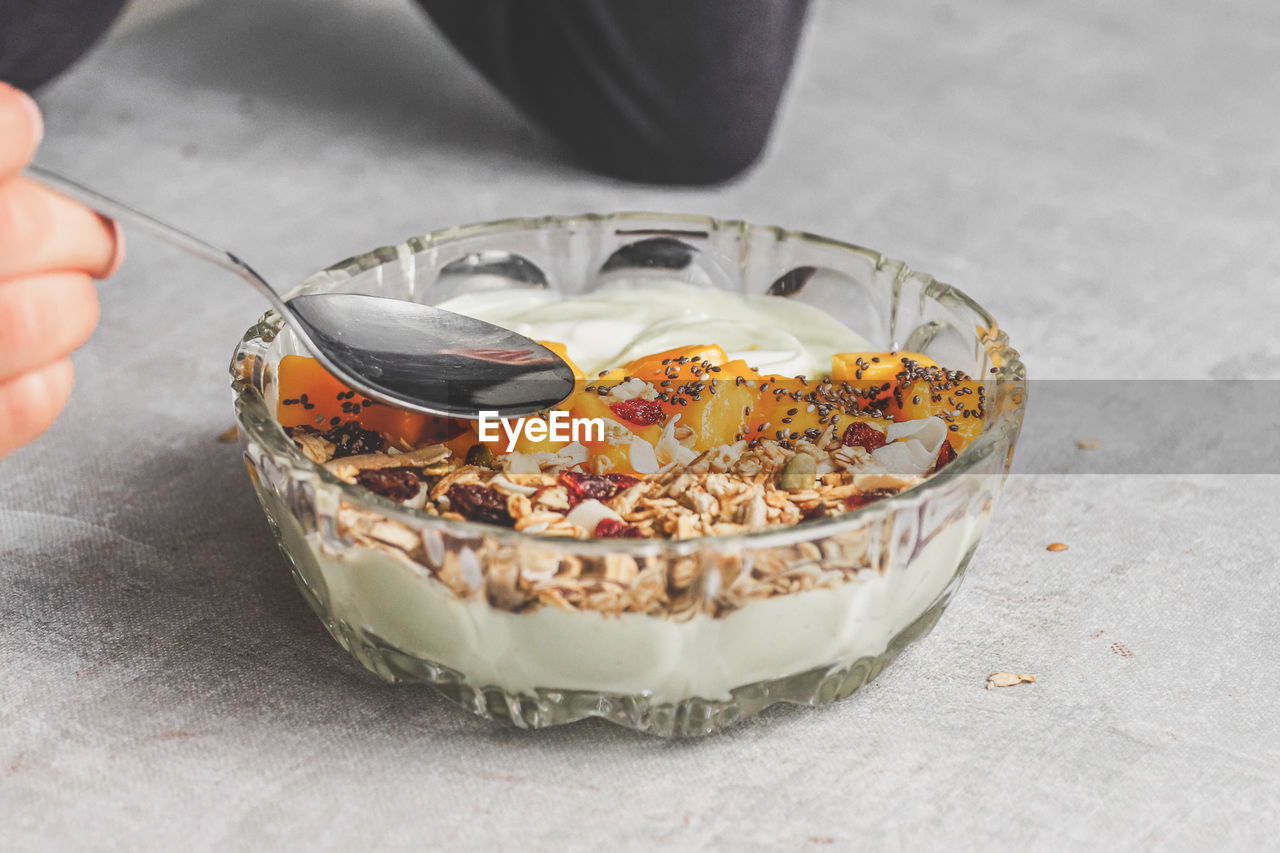 Close-up of hand holding spoon eating mango yoghurt avocado granola