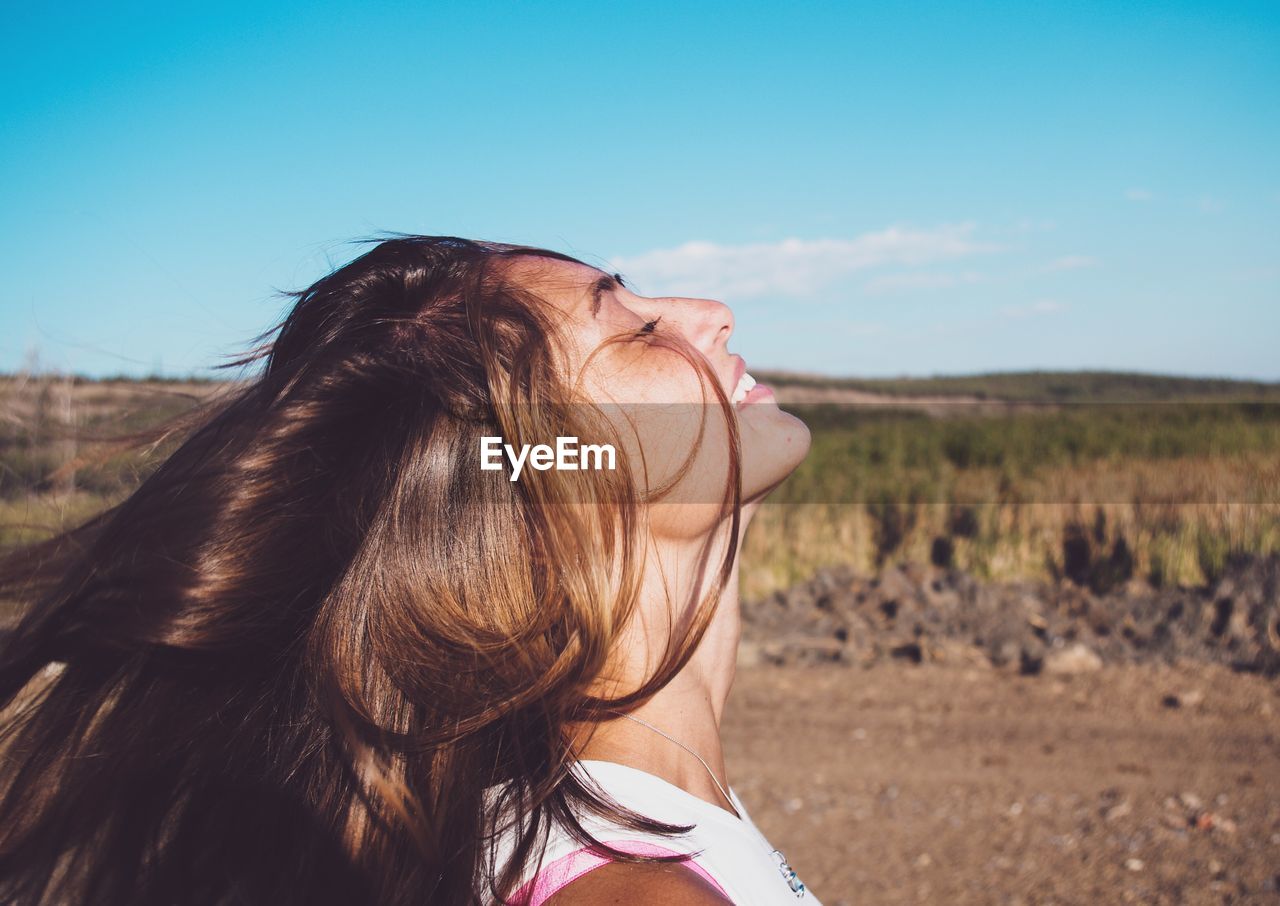 Teenage girl with eyes closed standing on field against sky