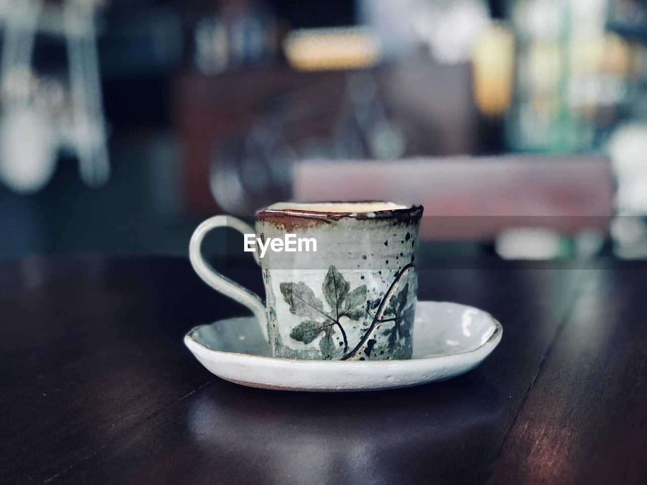 CLOSE-UP OF COFFEE CUP ON TABLE AGAINST CAFE