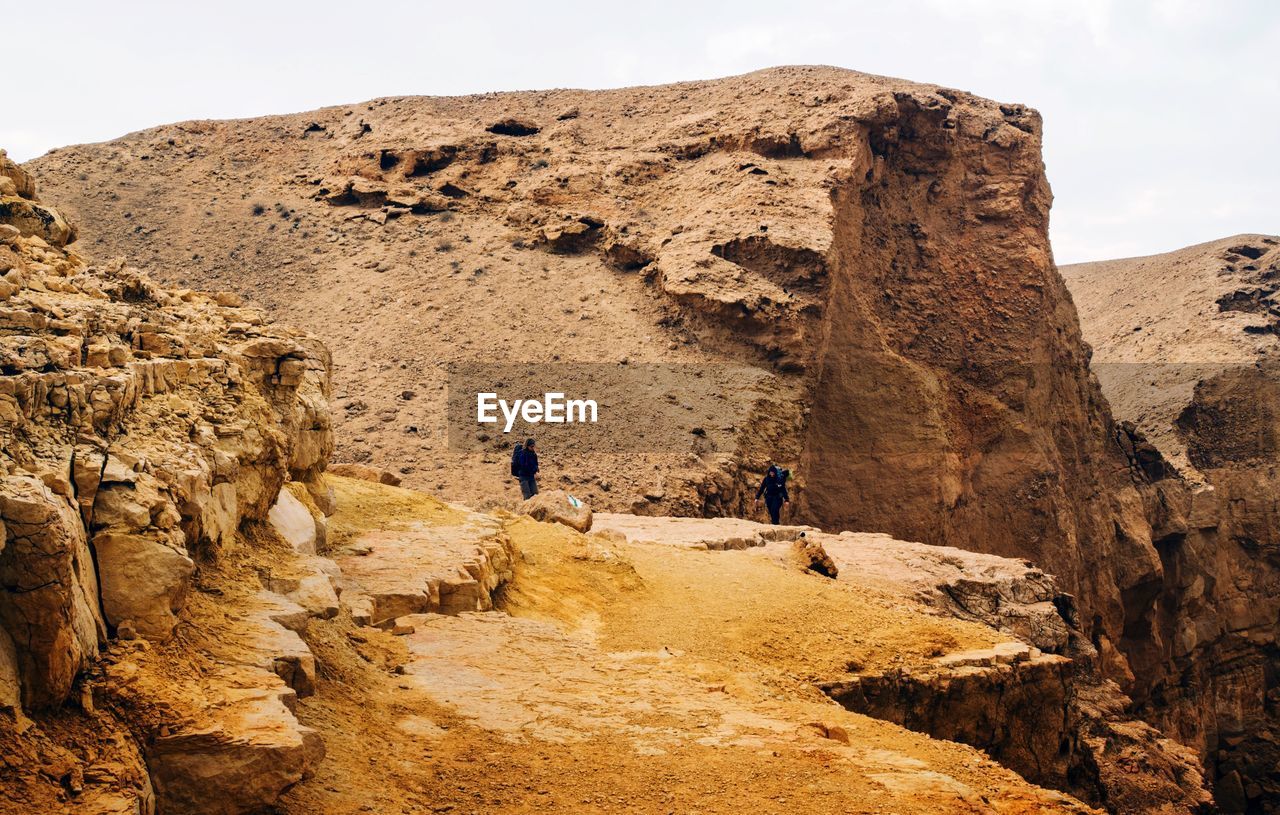 REAR VIEW OF MAN ON ROCK IN SAND