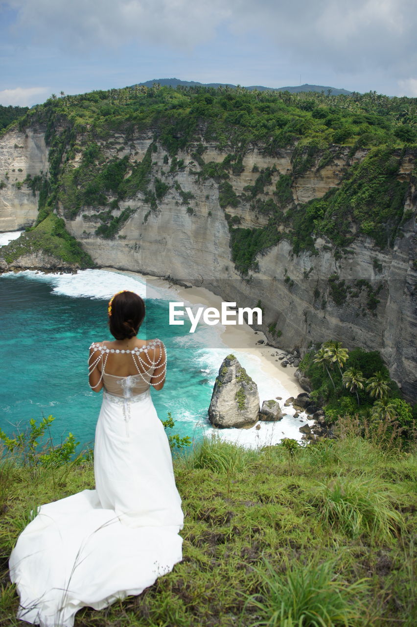 Rear view of bride standing on cliff against sea