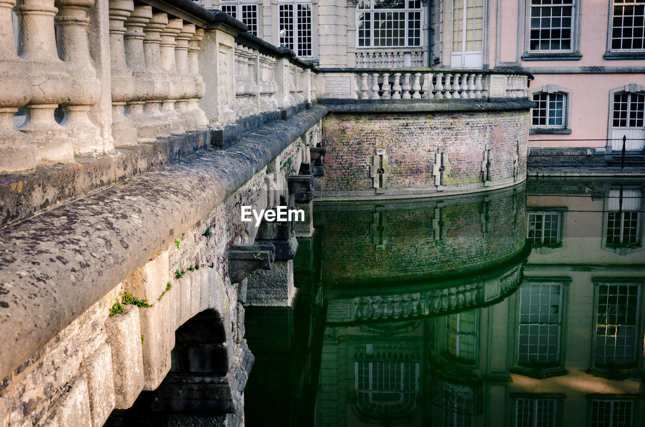 Historic building by bridge reflecting on canal in city