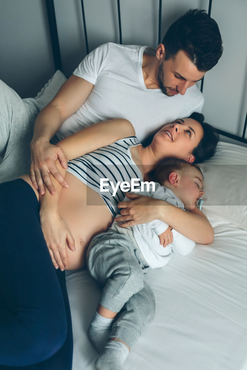 High angle view of pregnant woman with husband and son on bed at home