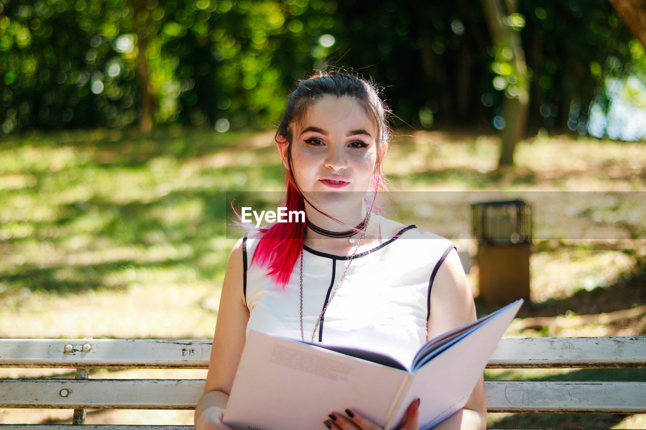 Woman holding file while sitting on bench at park