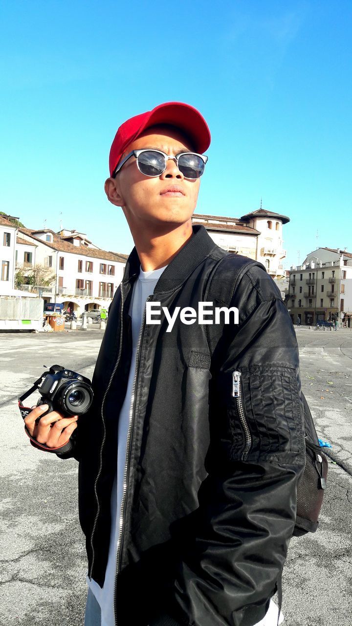 PORTRAIT OF MAN STANDING IN SUNGLASSES