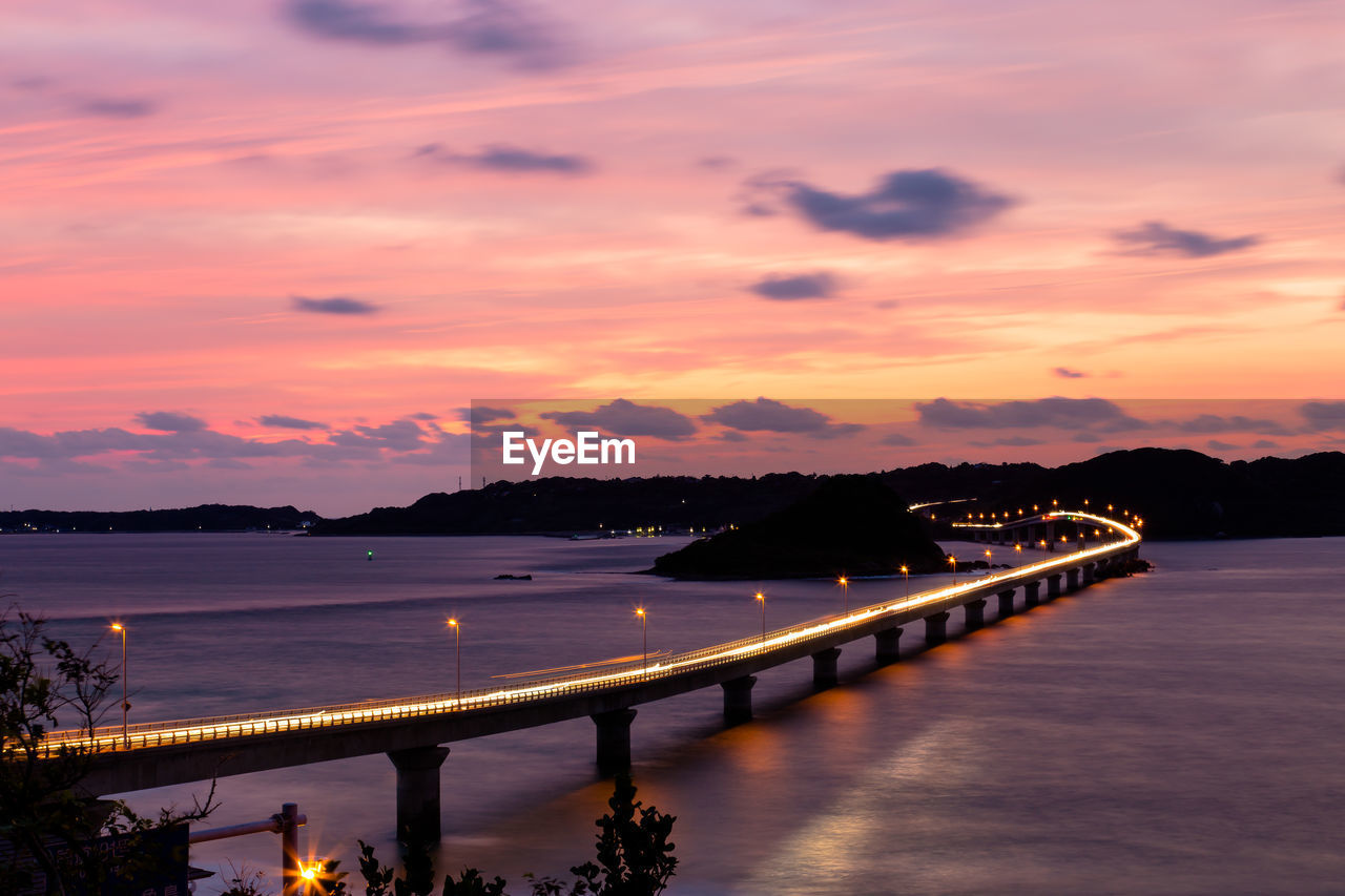 ILLUMINATED BRIDGE OVER SEA AGAINST SKY DURING SUNSET