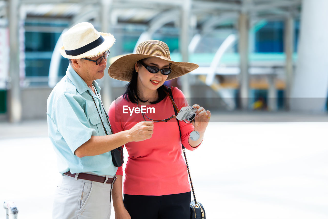 REAR VIEW OF WOMAN WEARING HAT HOLDING CAMERA