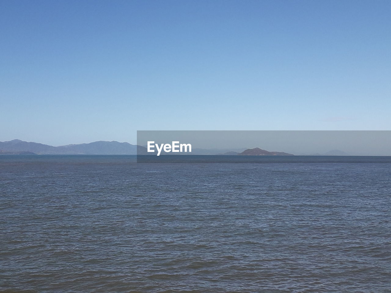 SCENIC VIEW OF SEA BY MOUNTAIN AGAINST CLEAR SKY