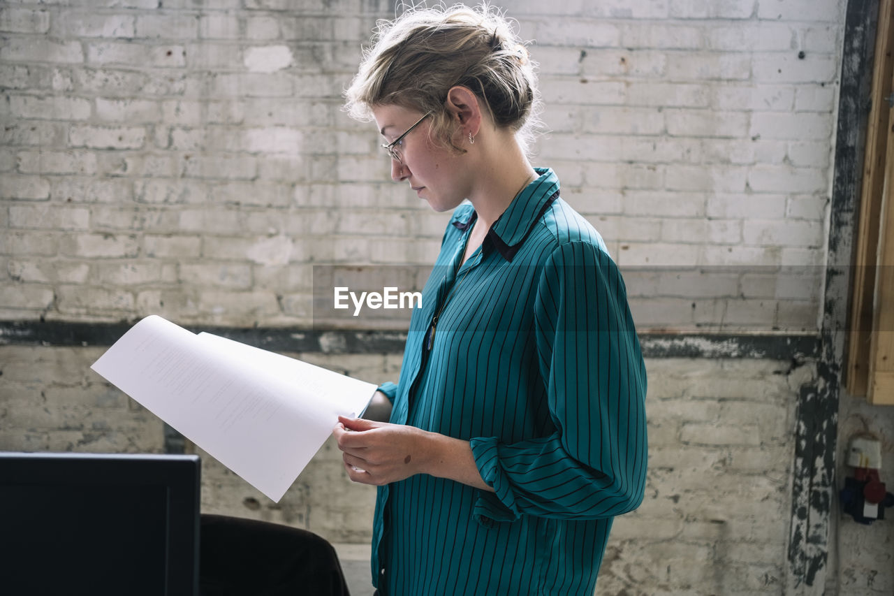 Confident young female it professional reading document standing at creative workplace