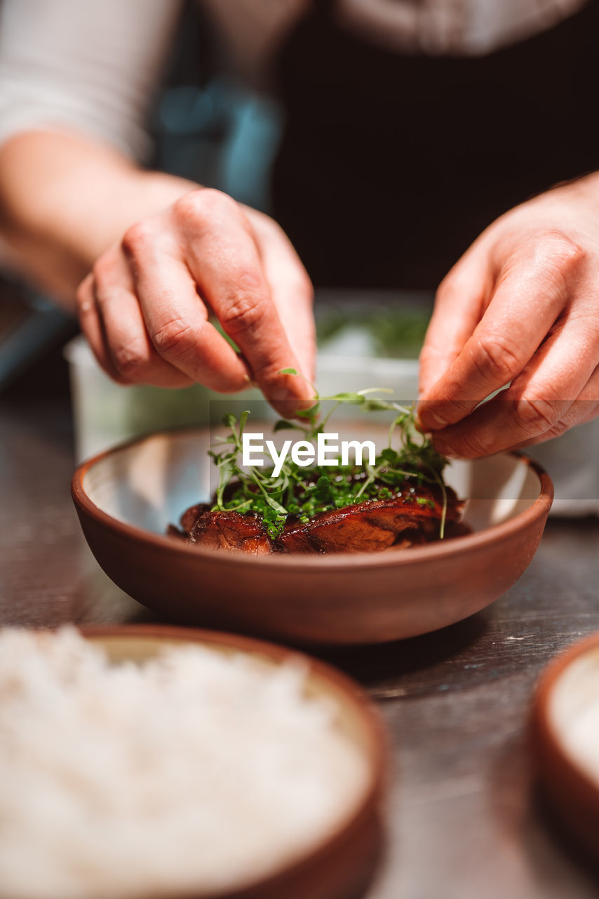 Vertical view of the unknown man chef hands decorating meat with herbs