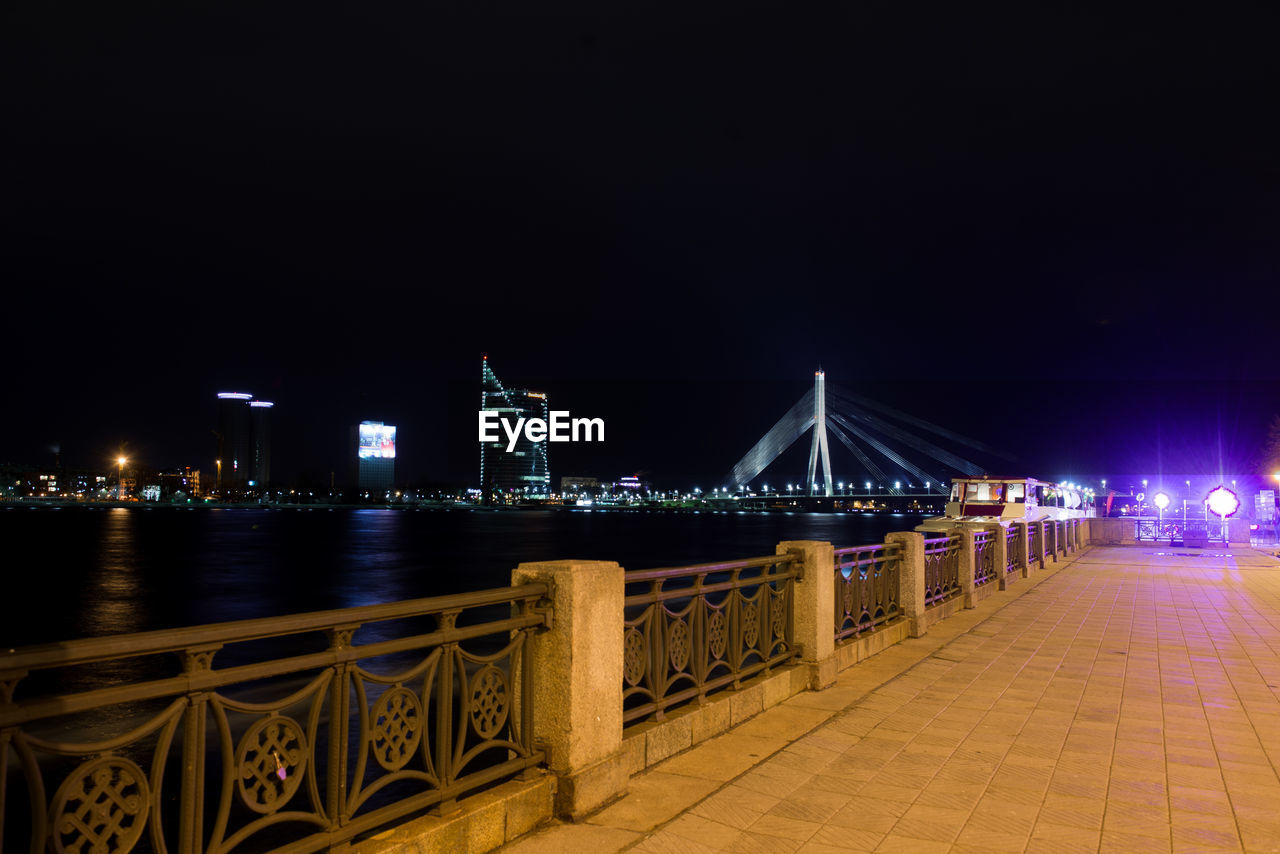 ILLUMINATED SUSPENSION BRIDGE OVER RIVER AGAINST SKY AT NIGHT