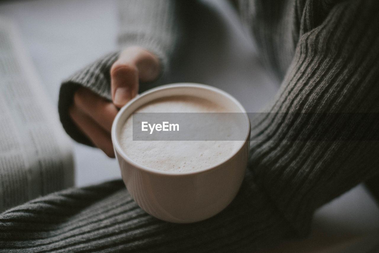 Midsection of person holding coffee cup on table