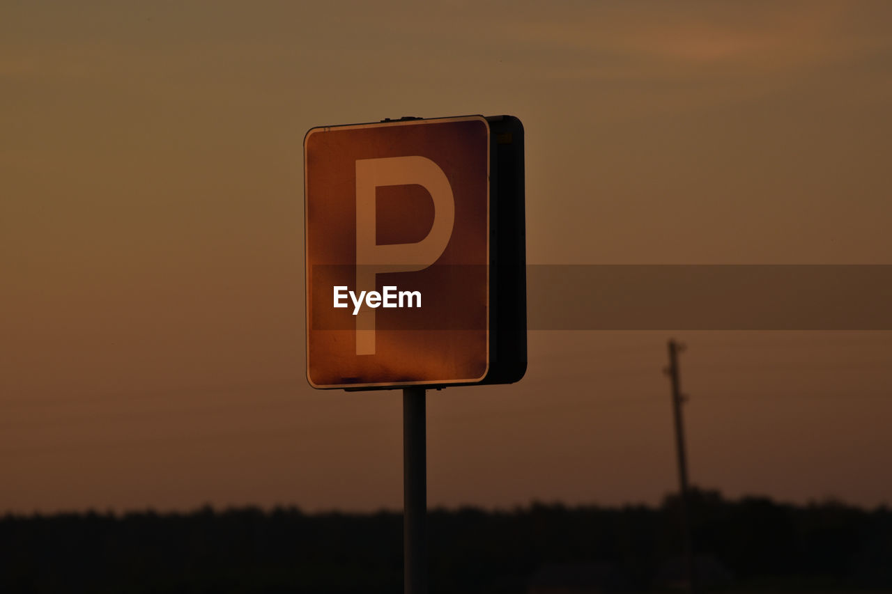 Close-up of road sign against sky during sunset