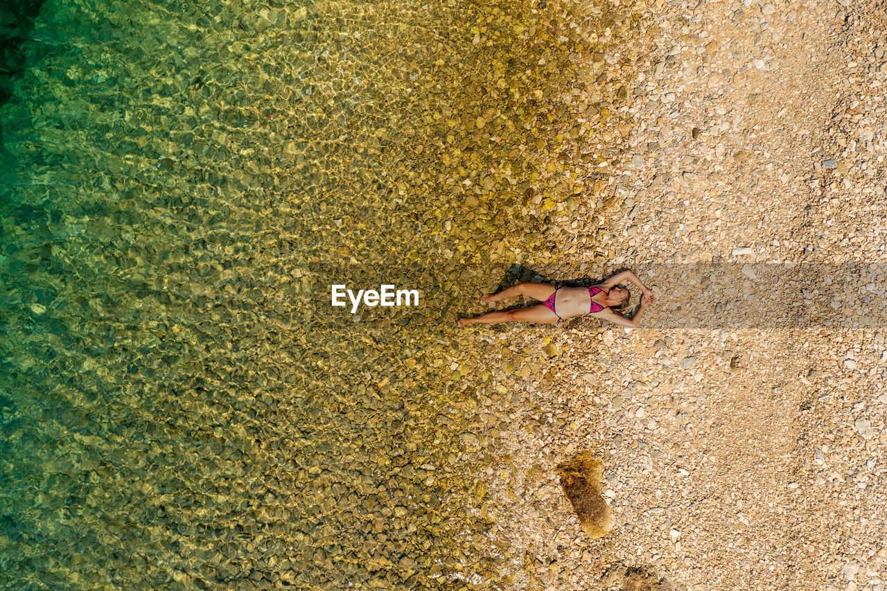 Aerial view of a girl having a sunbath on the pebble beach in the adriatic sea, croatia