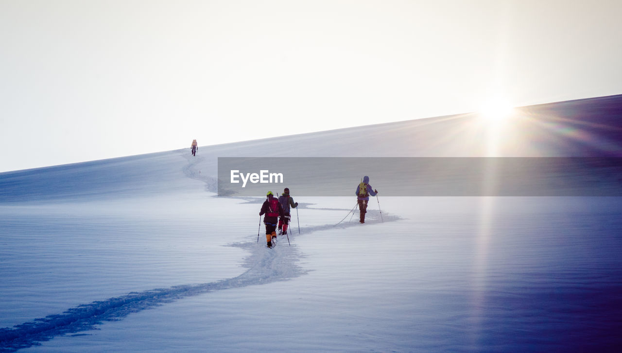 People skiing on mountain against clear sky during winter 