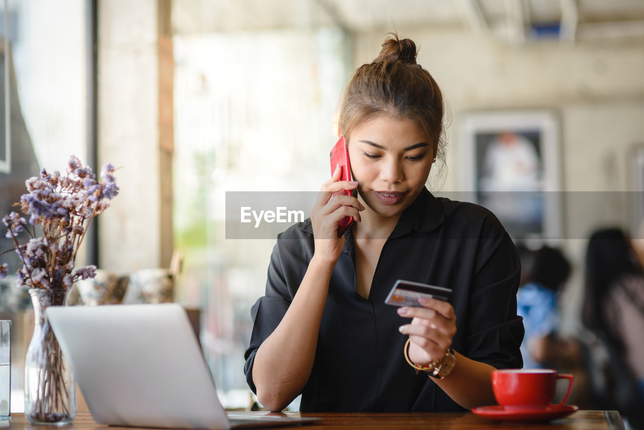 Woman talking on mobile phone while sitting at table in restaurant