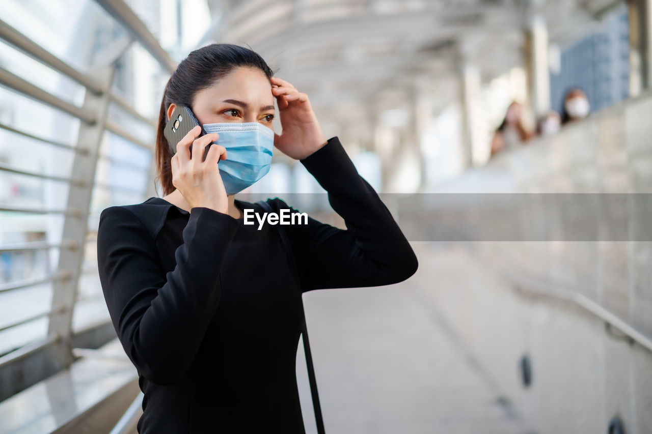 Businesswoman wearing mask talking on phone while standing on footbridge