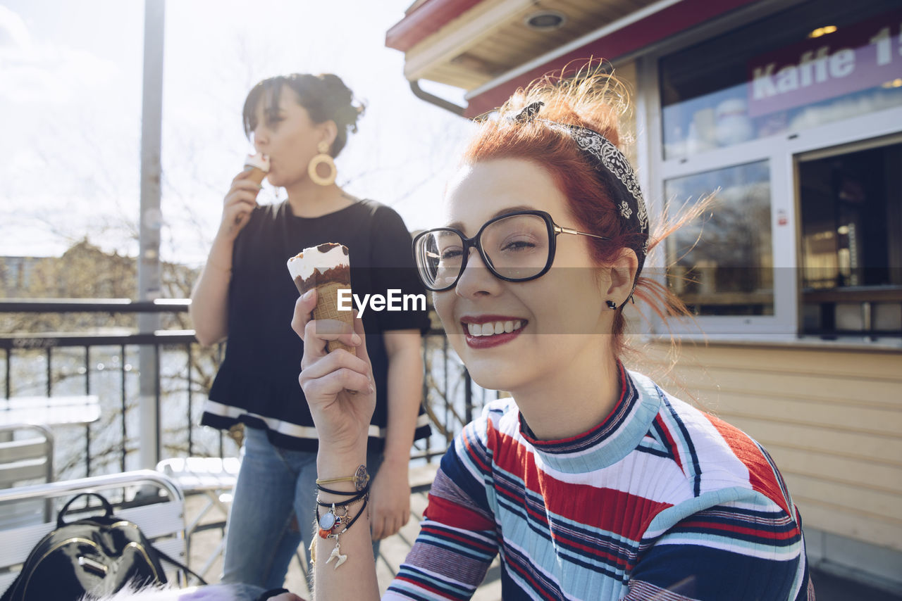 Hipster female friends eating ice cream by shop