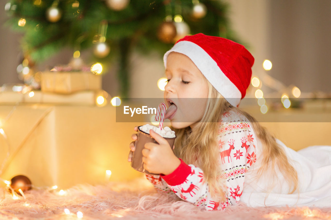 Cute girl holding hot chocolate while lying down on floor at home