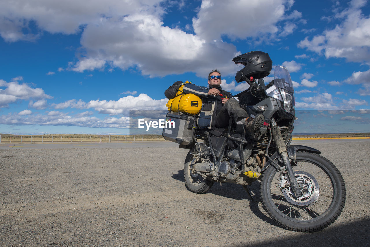 Man resting on his parked motorbike on a sunny day in patagonia, chile