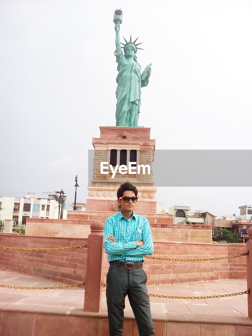 MAN STANDING AGAINST STATUE IN CITY AGAINST SKY IN BACKGROUND