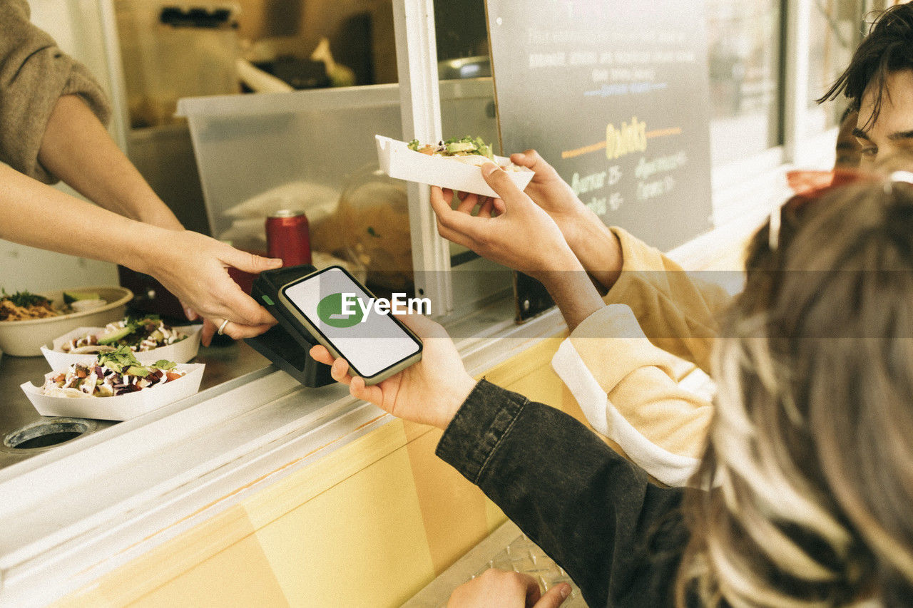 Woman paying via tap to pay method through smart phone while buying food from concession stand