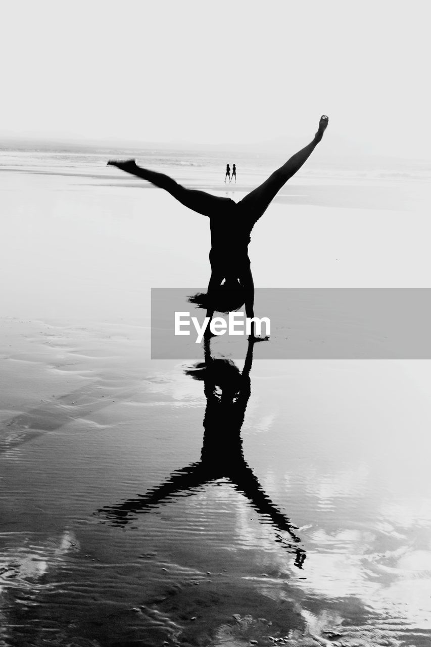 Silhouette woman doing cartwheel in sea against sky