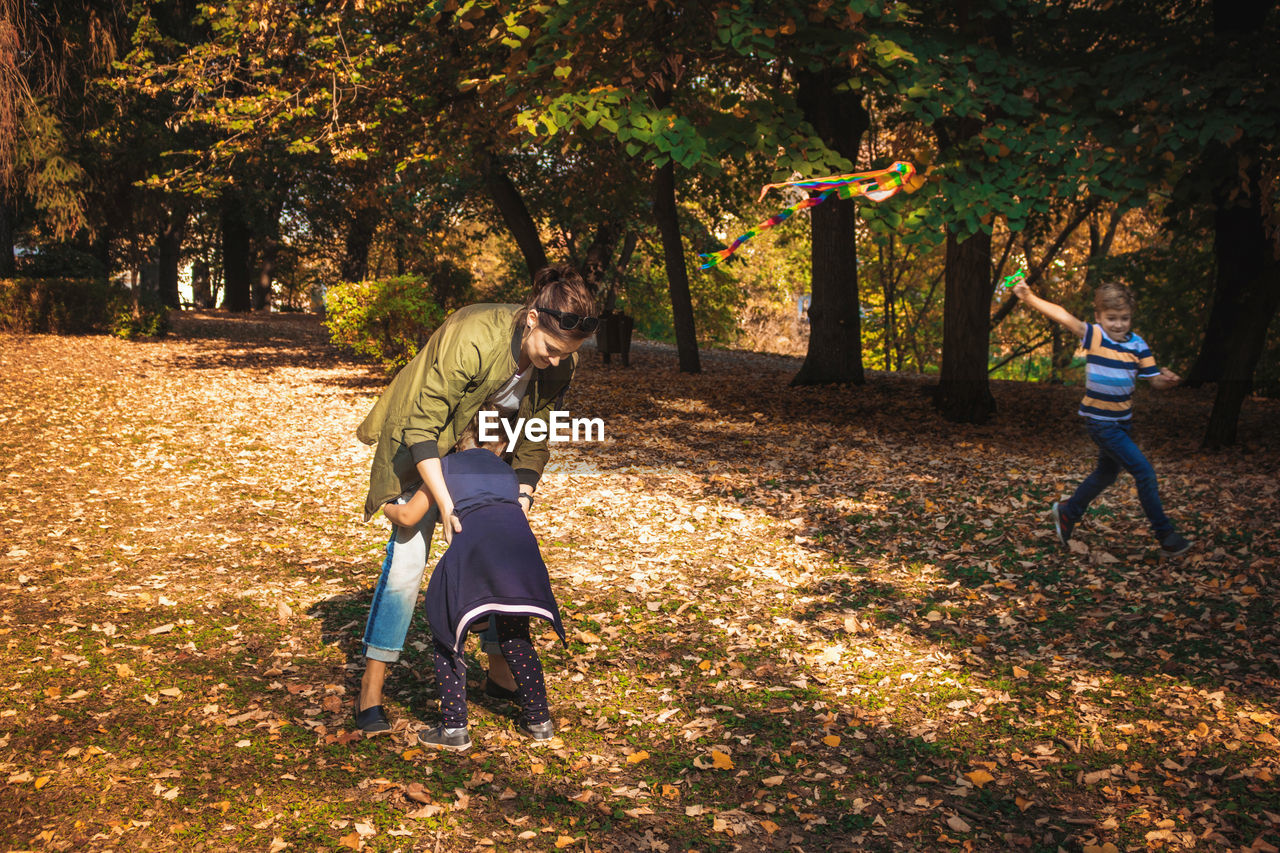 Woman playing with daughter by son running with kite in park during autumn