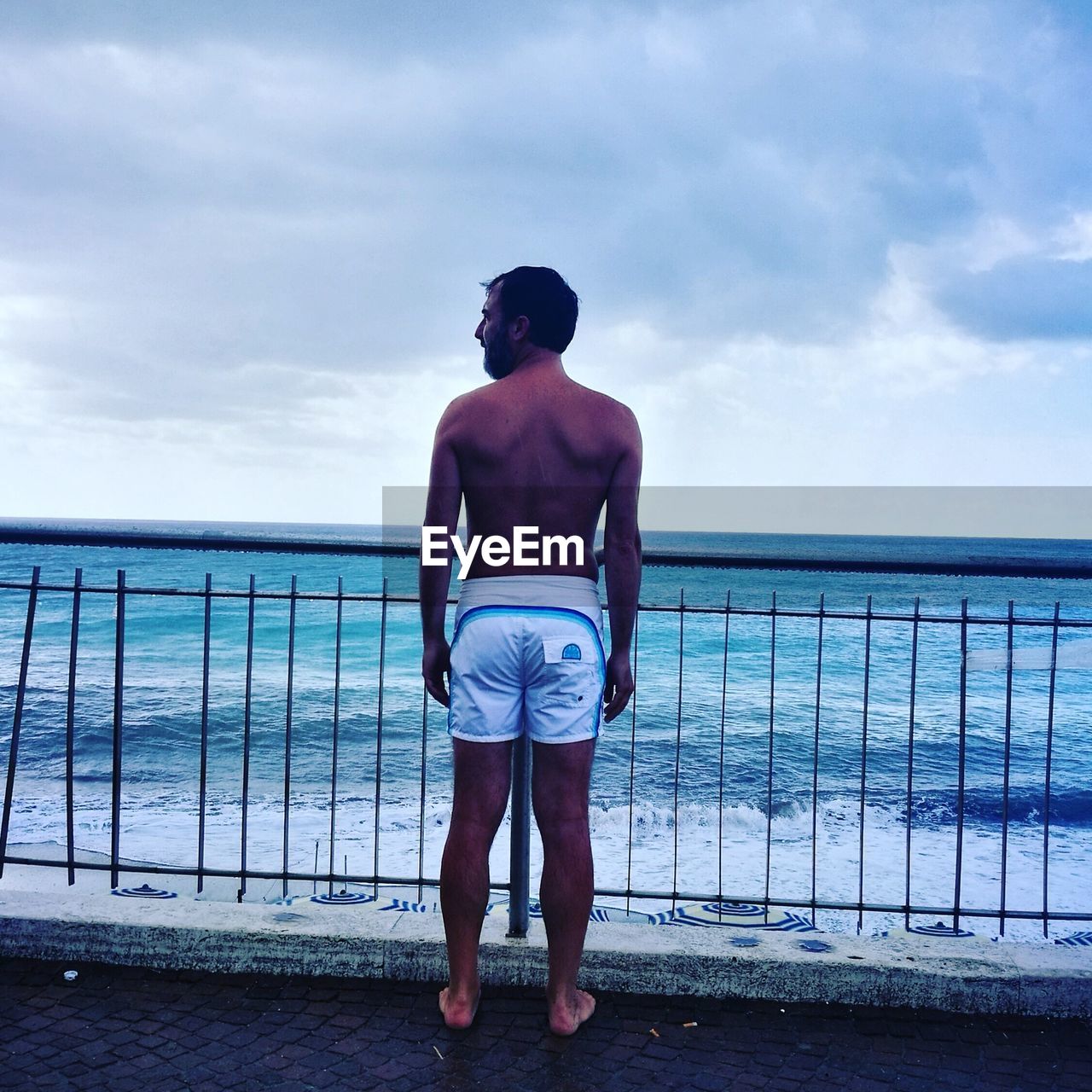 Rear view of shirtless man standing on bridge against sea