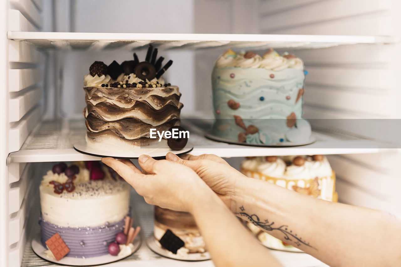 Unrecognizable woman putting fresh tasty cake with creative decorations in refrigerator while working in bakery