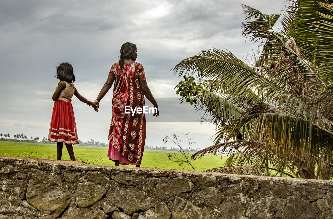 REAR VIEW OF PEOPLE STANDING BY PALM TREES