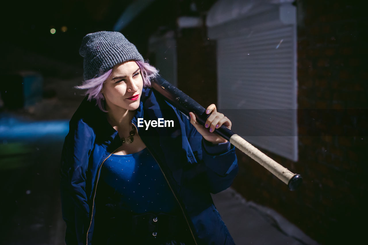 Young woman with baseball bat standing outdoors at night